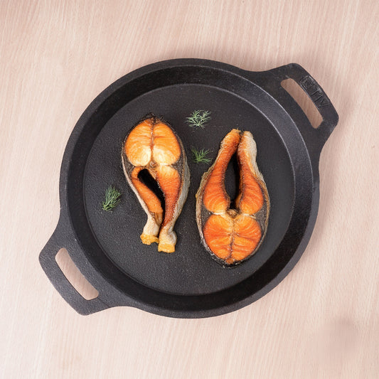 Two pieces of salmon in a black cast iron skillet on a light wooden surface