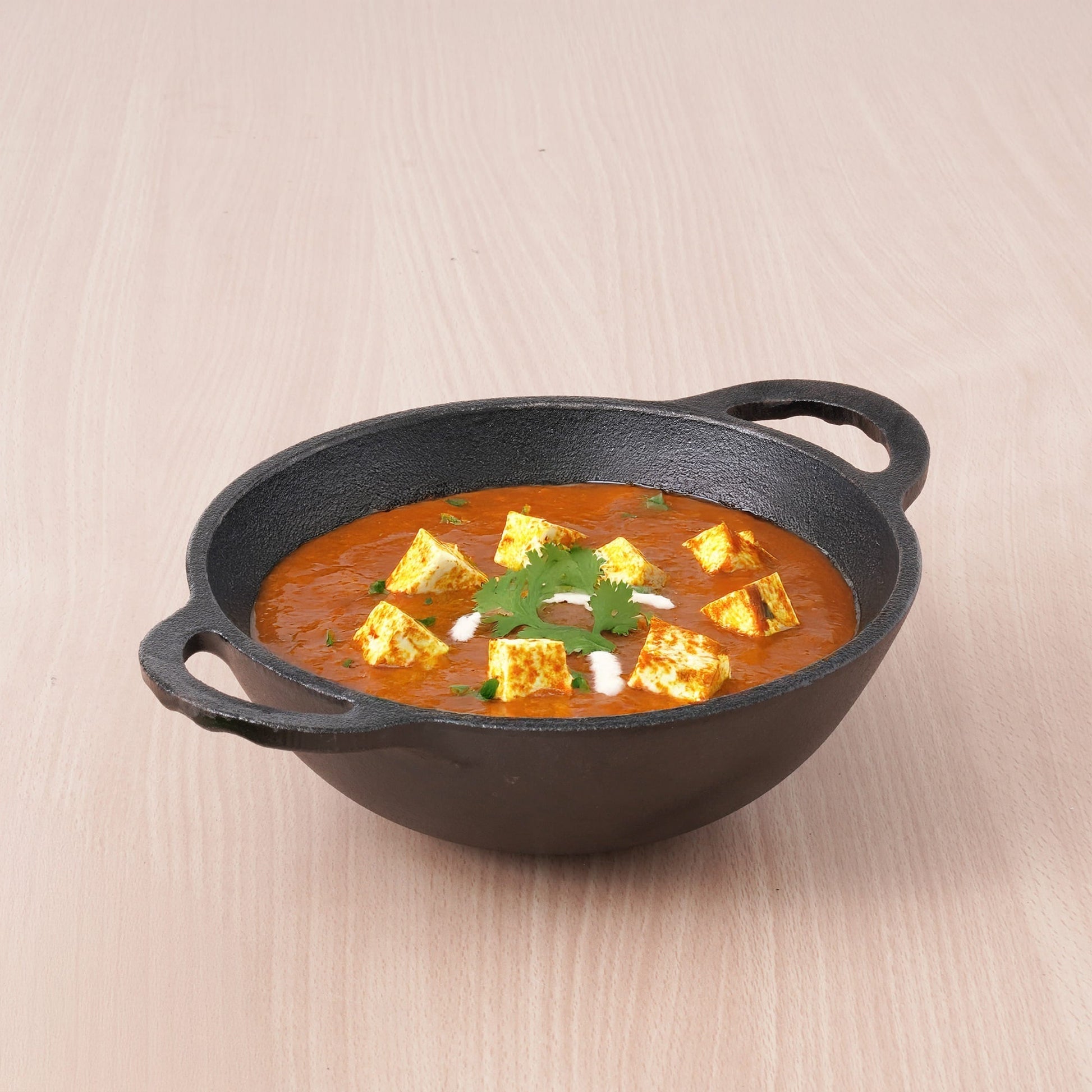 Dish of curry with tofu in a black cast iron skillet on a beige background