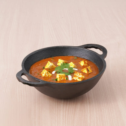 Dish of curry with tofu in a black cast iron skillet on a beige background