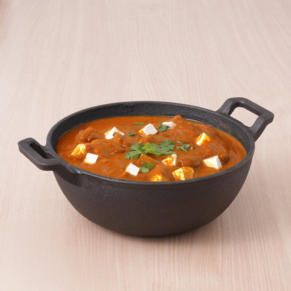 Black cast iron pot with a red curry dish on a beige background