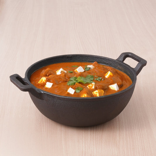 Black cast iron pot with a red curry dish on a beige background