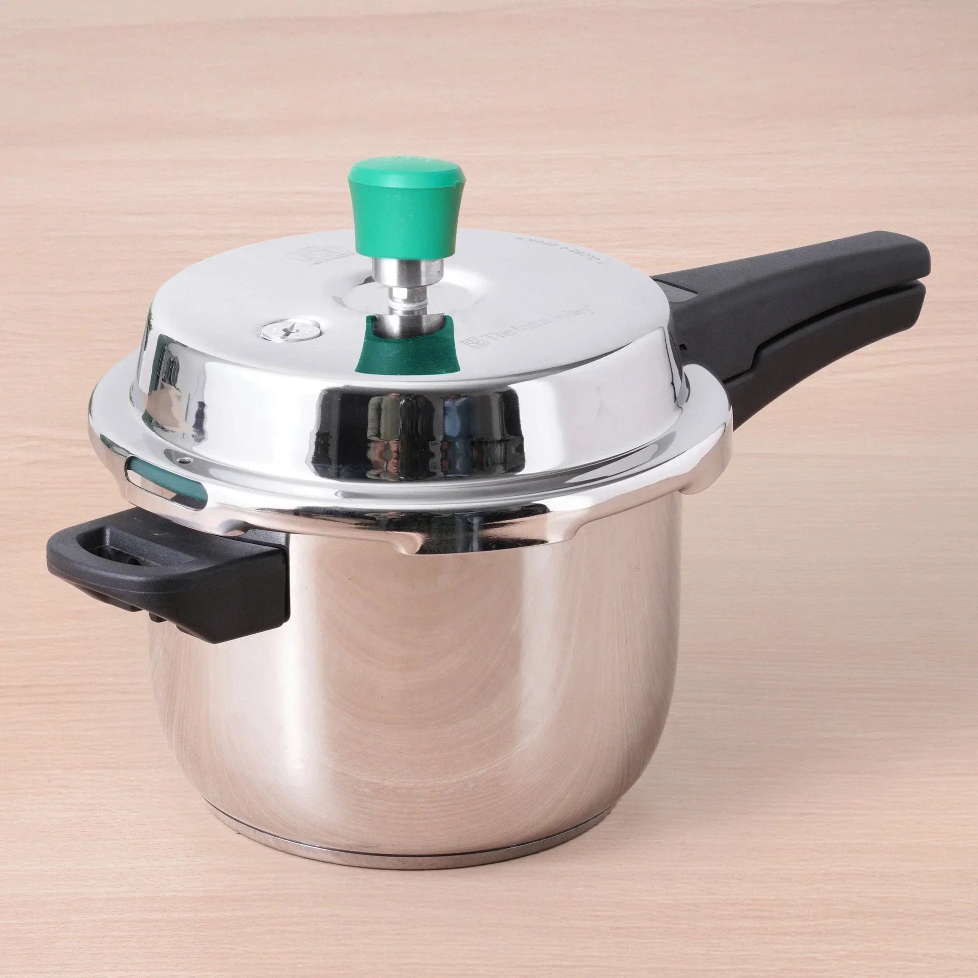 Stainless steel pressure cooker with a green handle on a beige background