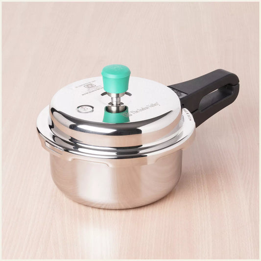 Stainless steel pressure cooker with a green handle on a beige background