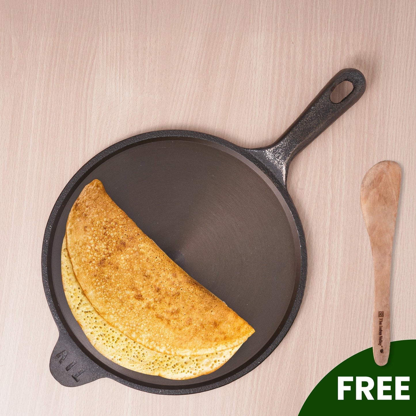 Cast iron skillet with a cooked crepe and a wooden spatula on a light wood background