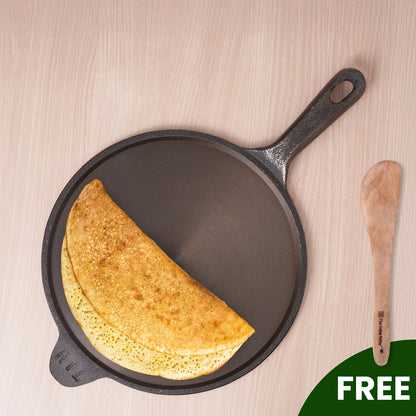 Cast iron skillet with a cooked crepe and a wooden spatula on a light wood background