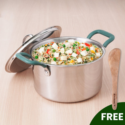 Stainless steel pot with green handles containing a vegetable stir-fry on a wooden surface.