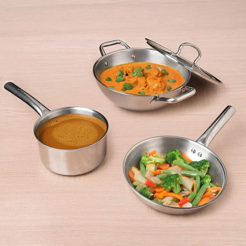 Three stainless steel cookware items with different dishes on a beige background