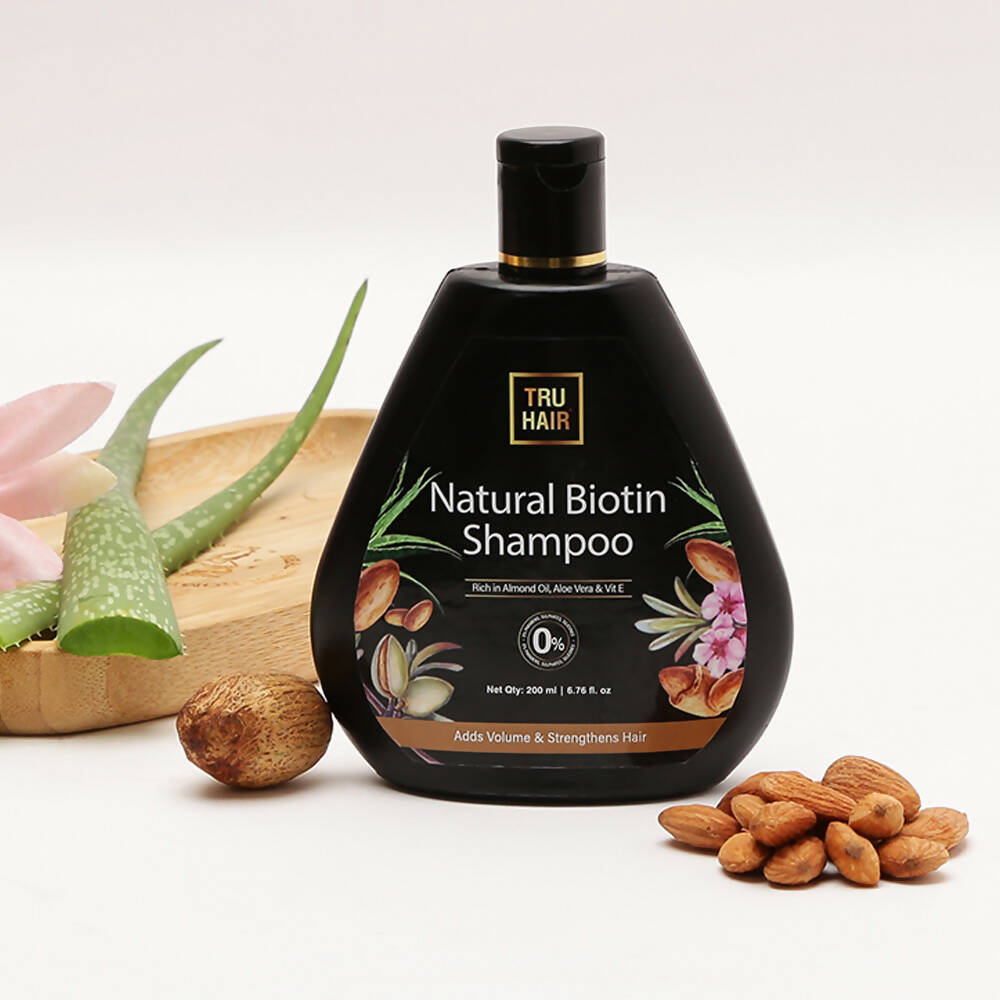 Black shampoo bottle labeled 'Natural Biotin Shampoo' with a decorative label featuring almonds and aloe vera on a white background.