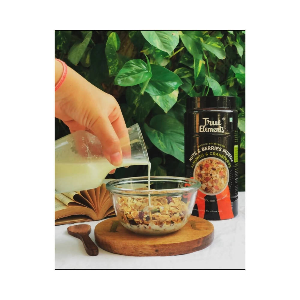 Hand pouring milk into a bowl of cereal with a container of 'True Elements' cereal in the background.