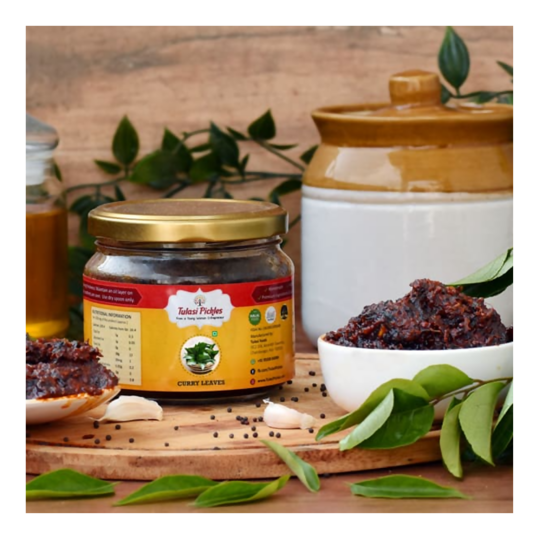 Jar of curry leaves with a bowl of curry leaves on a wooden surface with green leaves.