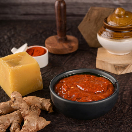 Red sauce in a black bowl with cheese and ginger on a wooden surface