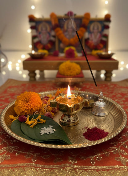 Decorative setup with lit candle, flowers, and incense on a tray in front of a blurred altar.