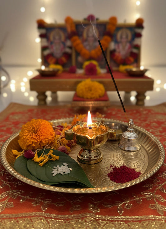 Decorative setup with lit candle, flowers, and incense on a tray in front of a blurred altar.