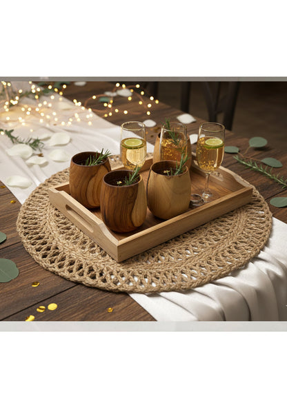 Wooden tray with glasses of a golden beverage on a woven mat outdoors.